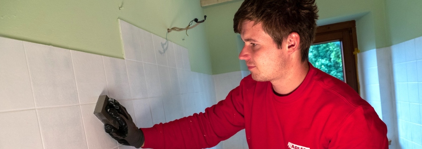 Een persoon is muurtegels in een badkamer aan het opschuren